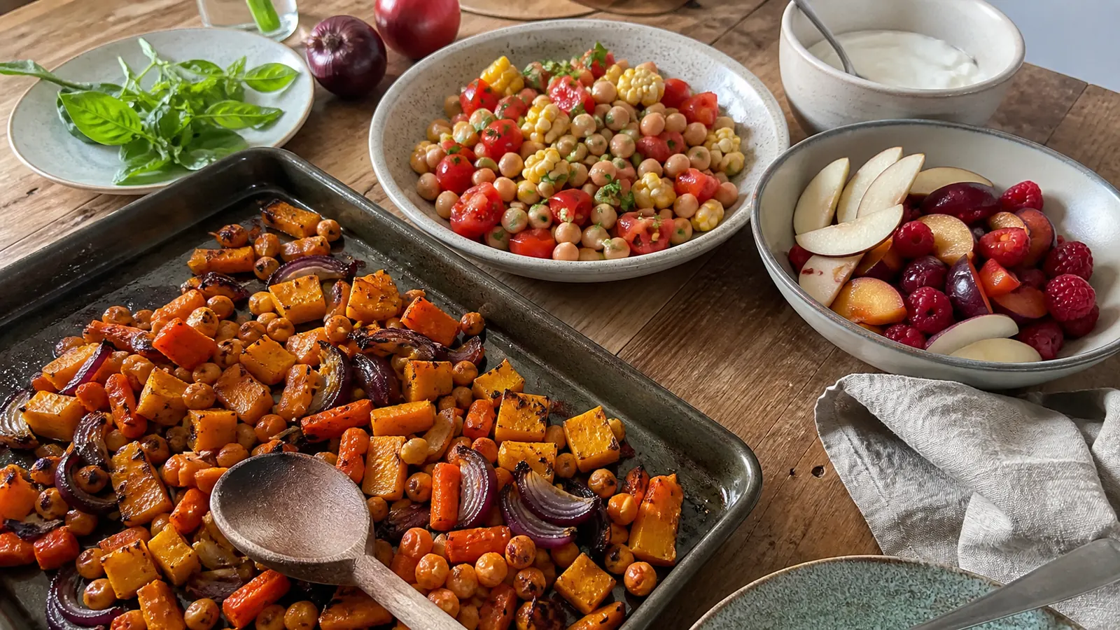 Roasted squash, carrots, red onion and chickpeas beside a tomato, corn and bean salad and a bowl of pears, plums and raspberries
