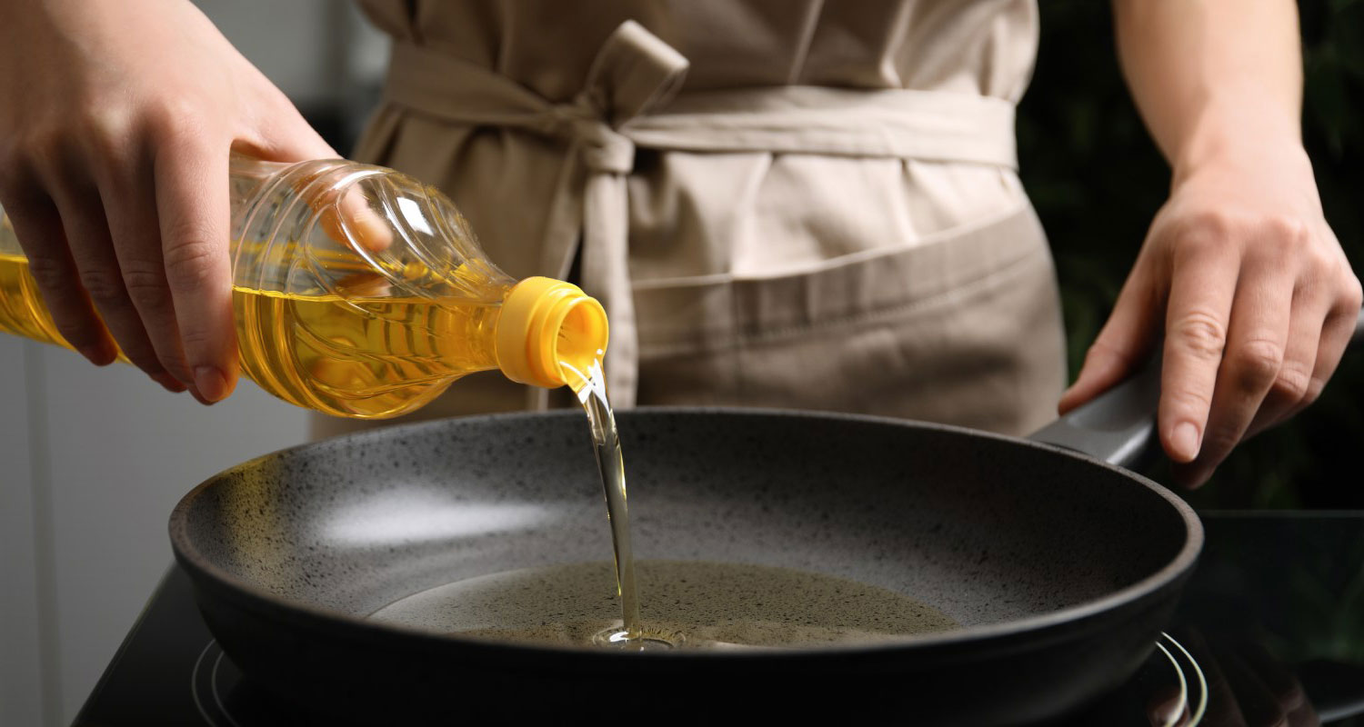 Woman pouring cooking oil from bottle into frying pan